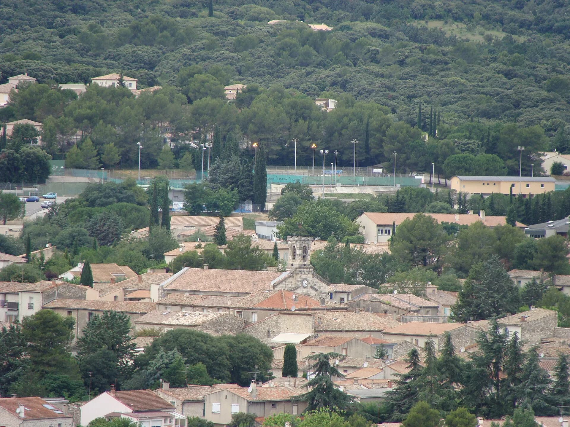 Le centre de Saint-Gély-du-Fesc, ses toits de tuiles et la garrigue boisée derrière