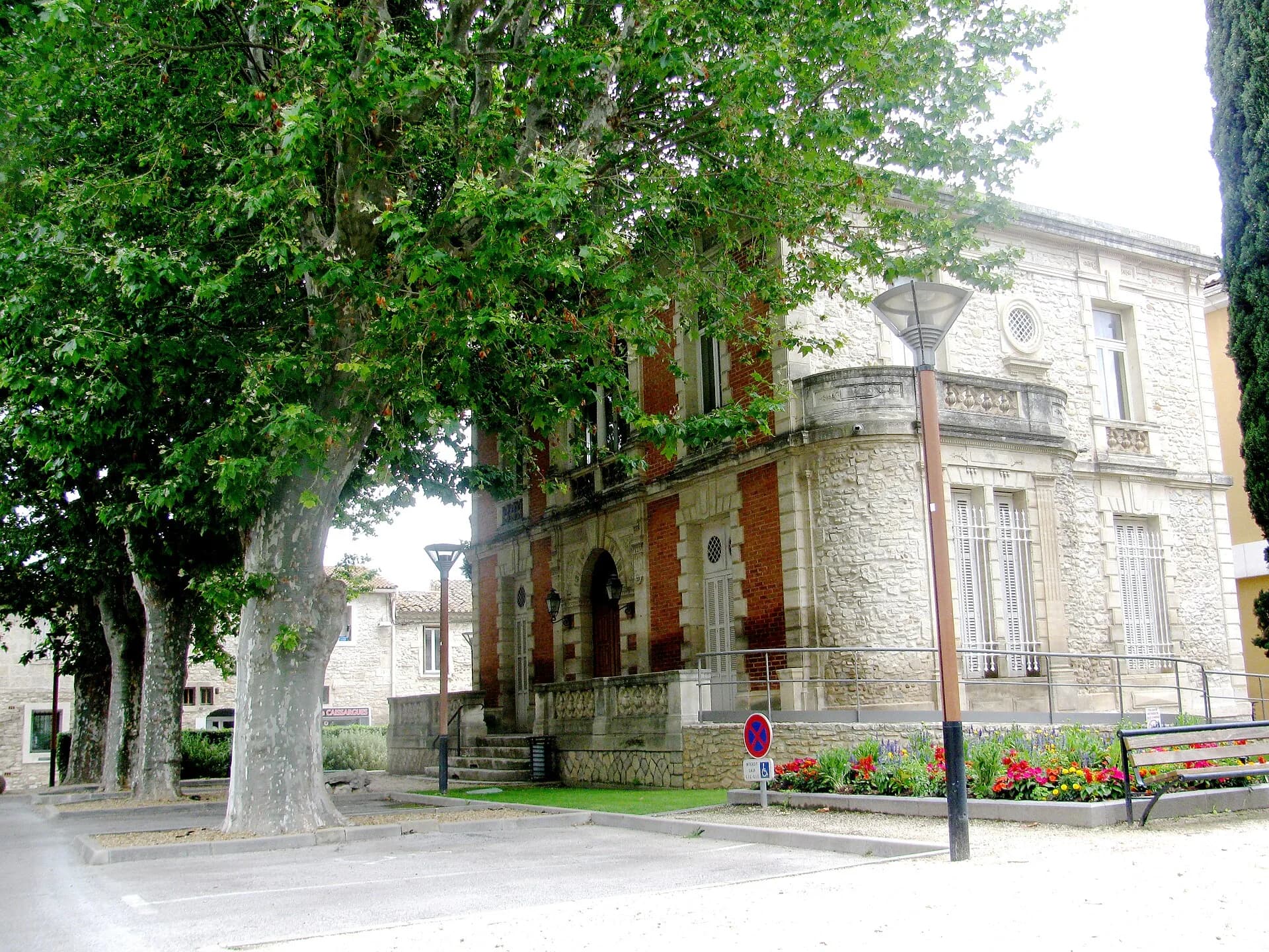 La mairie de Caissargues en pierre et brique, son bow-window a balustrade et les platanes de la place