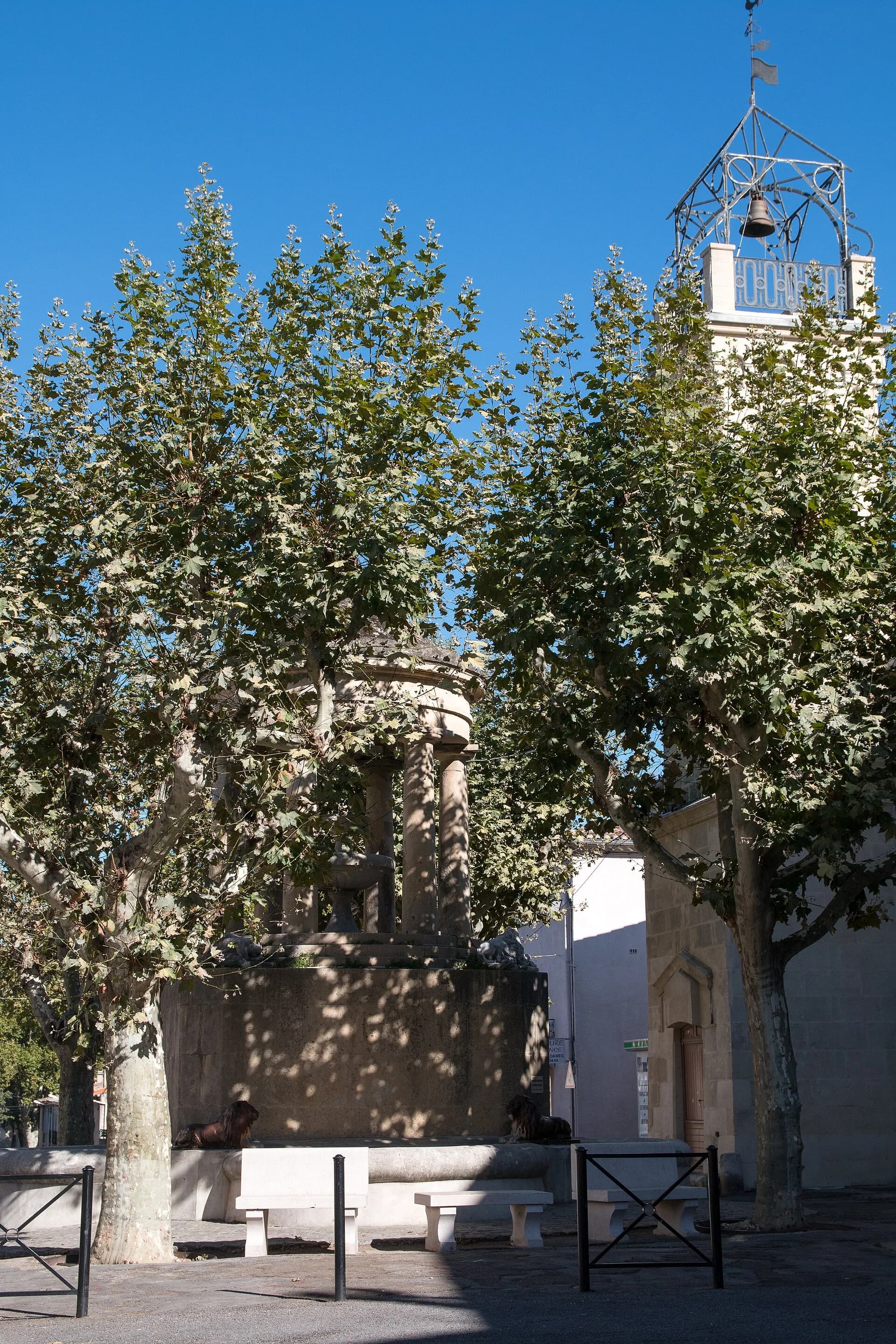 La place de Clarensac, ses platanes, la fontaine La Griffe et la tour de l'Horloge