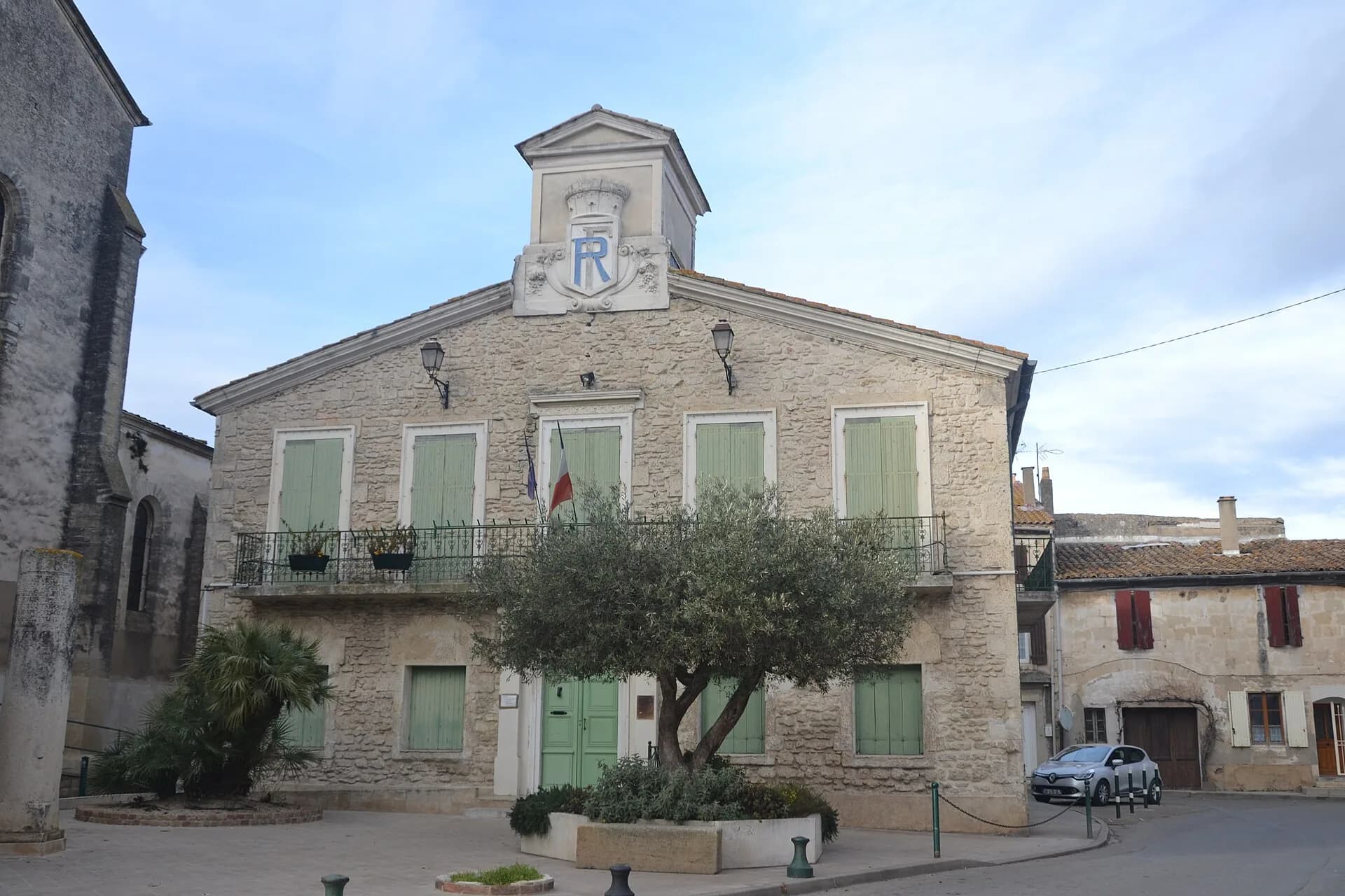 La mairie de Manduel en pierre de taille, ses volets vert d'eau et l'olivier de la place