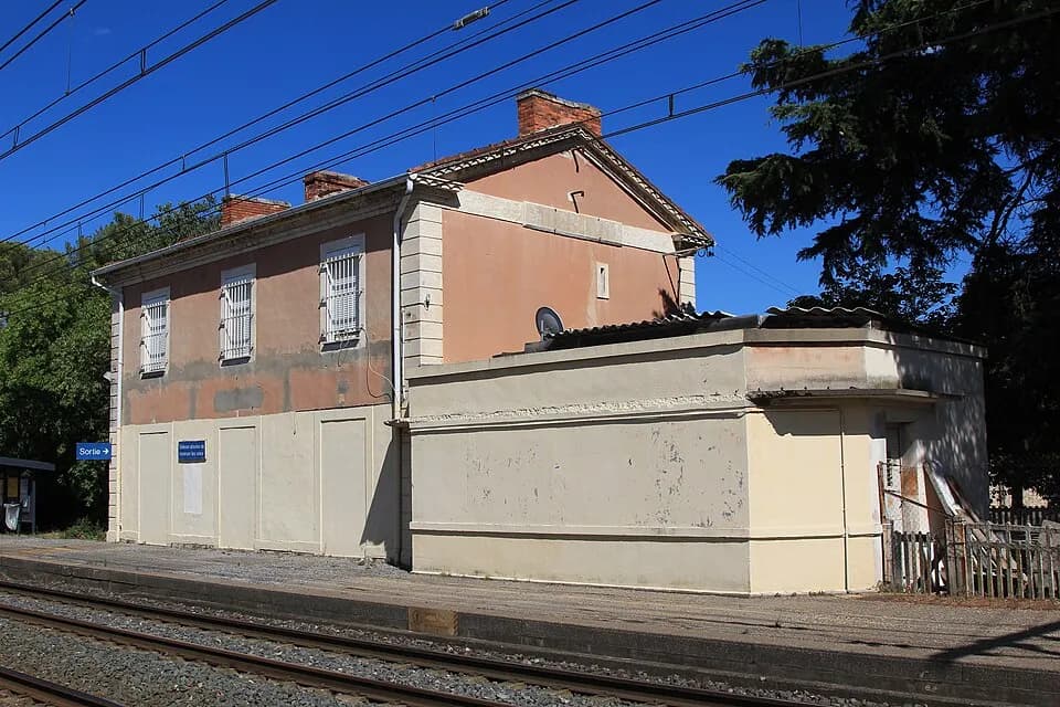L'ancien batiment voyageurs de la gare de Milhaud, sa facade ocre et les voies au premier plan