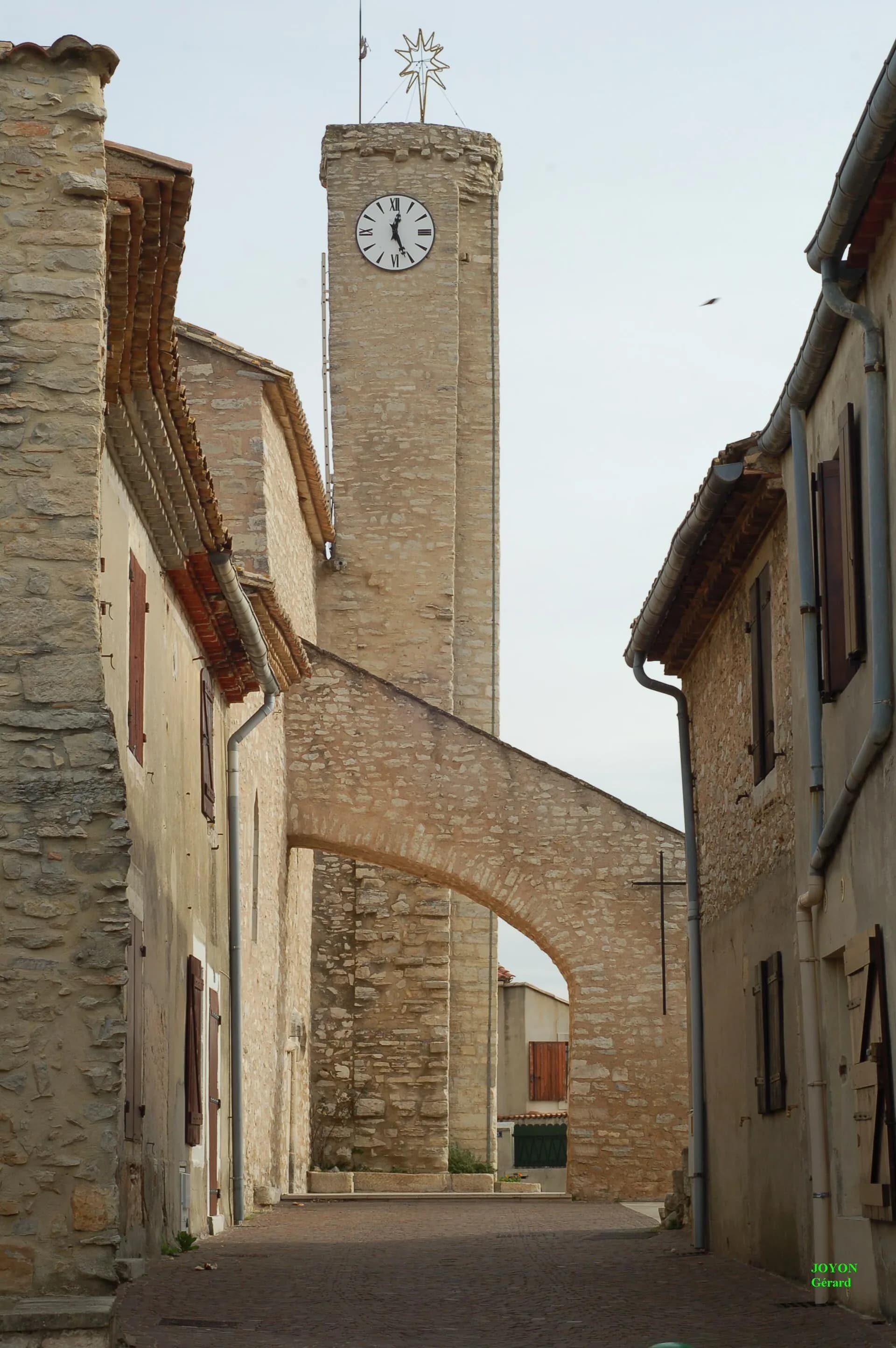 Une ruelle en pierre de Poulx, l'arc-boutant et la tour de l'horloge de l'église Saint-Michel